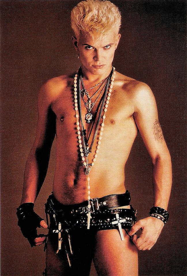 Billy idol staring at the camera wearing nothing but a bunch of belts and crosses